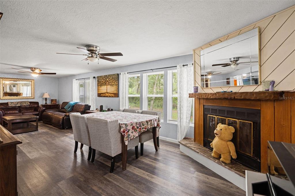 A living and dining area features wood-look flooring, a fireplace with a teddy bear, and furniture — 8343 YELLOW PINE AVENUE, BROOKSVILLE, FL