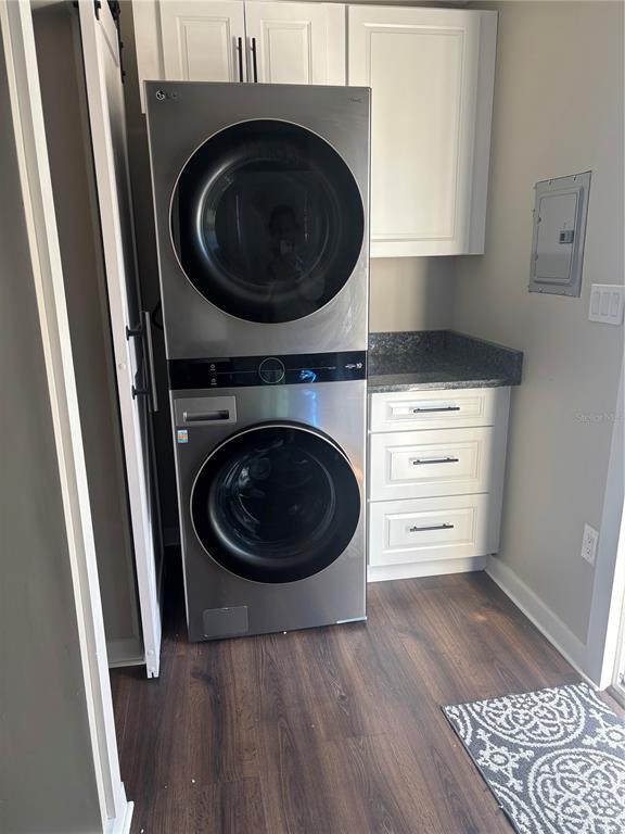 A laundry room features a stacked washer-dryer unit, white cabinets, and dark wood-look flooring — 20285 US HWY 27 UNIT 103, CLERMONT, FL