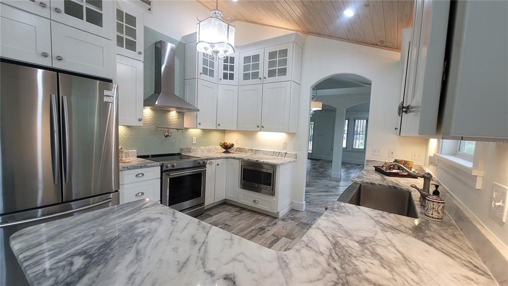 A kitchen features white cabinetry, marble countertops, stainless steel appliances, and a wood-paneled ceiling — 1837 HOLLENBECK DRIVE, ORLANDO, FL