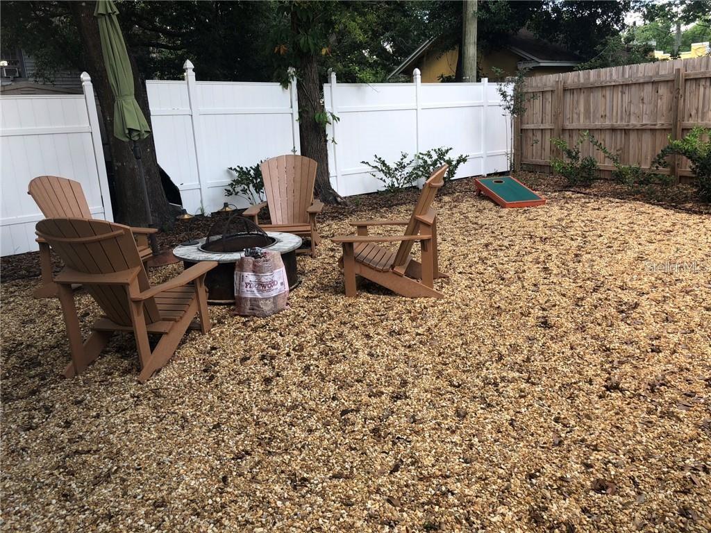 A backyard features a gravel patio with a fire pit, Adirondack chairs, and a cornhole board — 1837 HOLLENBECK DRIVE, ORLANDO, FL