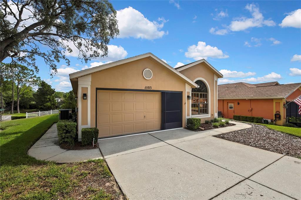 A tan single-story house features a two-car garage, a concrete driveway, and a arched window — 11103 CHERRYWOOD COURT, SPRING HILL, FL