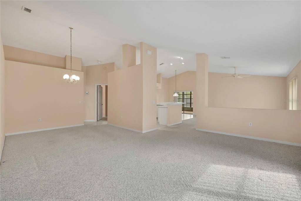 A spacious, carpeted living area features vaulted ceilings, neutral walls, and an open kitchen view — 11103 CHERRYWOOD COURT, SPRING HILL, FL