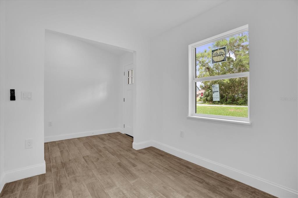 A bright, empty room with white walls, wood-look tile flooring, and a single window — 300 CHEROKEE AVENUE, ORANGE CITY, FL