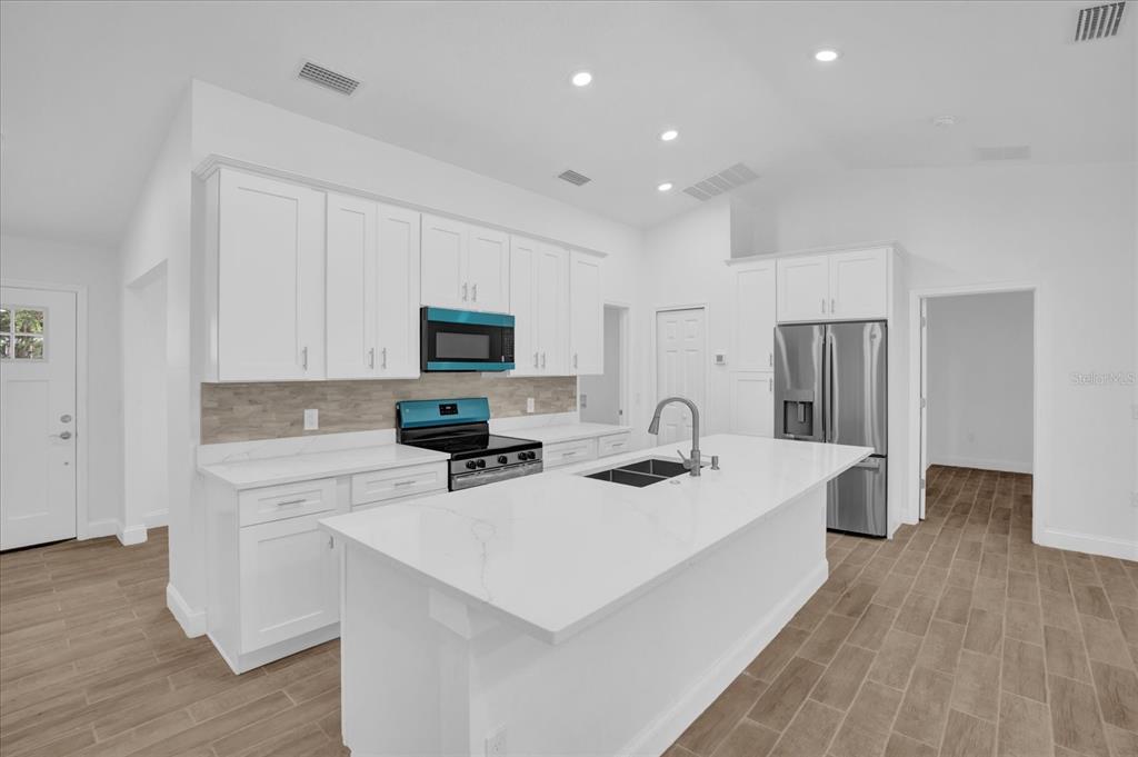 A modern kitchen features white cabinets, a large island with a sink, and stainless appliances — 300 CHEROKEE AVENUE, ORANGE CITY, FL