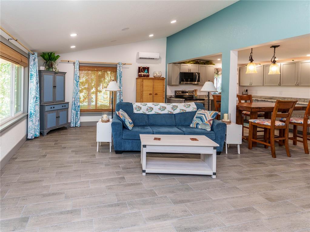A living room with blue furniture, wood-look tile flooring, and an open kitchen area — 4910 LIMESTONE DRIVE, PORT RICHEY, FL