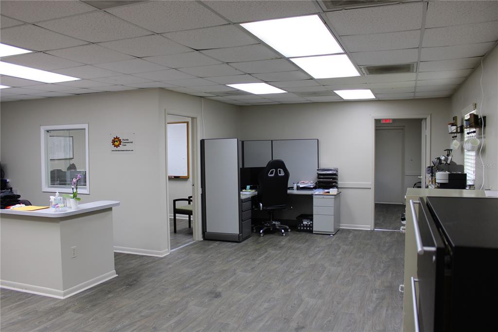 An office interior features a reception desk, a cubicle workstation, and a doorway leading to another room — 1158 ALTERNATE HWY 19 UNIT 1, HOLIDAY, FL