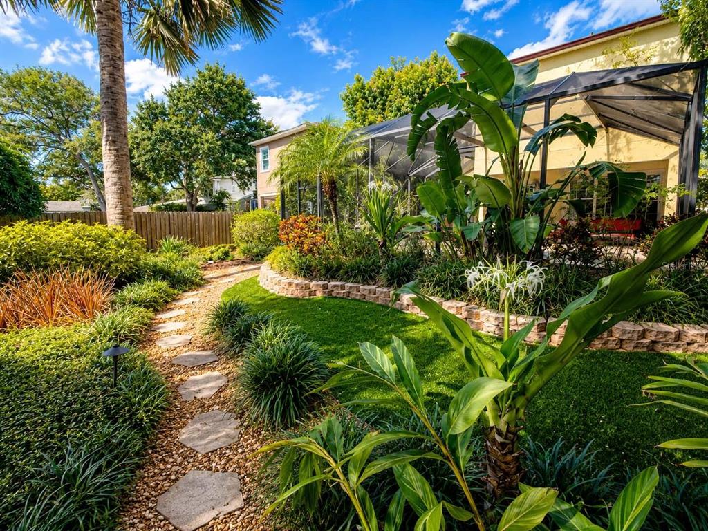 A stone path winds through a landscaped backyard with a screened-in pool enclosure — 5916 6TH STREET, TAMPA, FL