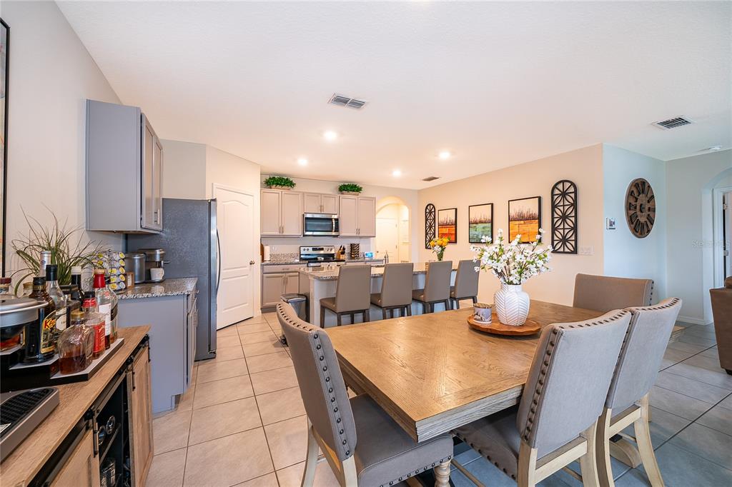 A dining area with a wooden table and chairs adjacent to a kitchen with gray cabinets — 1933 BELLKNOLL LANE, KISSIMMEE, FL