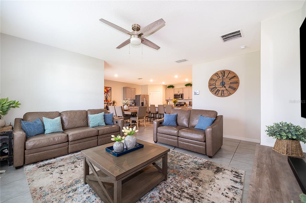 A living room with brown leather sofas, a wooden coffee table, and an open kitchen — 1933 BELLKNOLL LANE, KISSIMMEE, FL