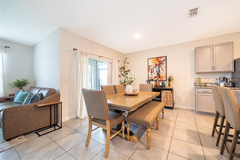 An open-concept dining area features a wooden table, upholstered chairs, a bench, and tile flooring — 1933 BELLKNOLL LANE, KISSIMMEE, FL