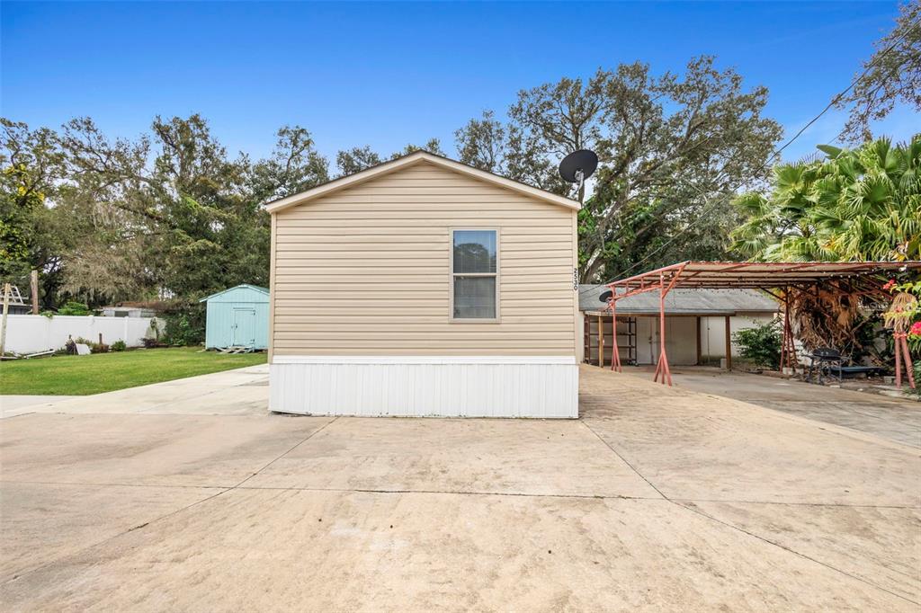 The exterior of a tan mobile home features a concrete driveway and a metal carport — 2530 CRESAP STREET, LAKELAND, FL