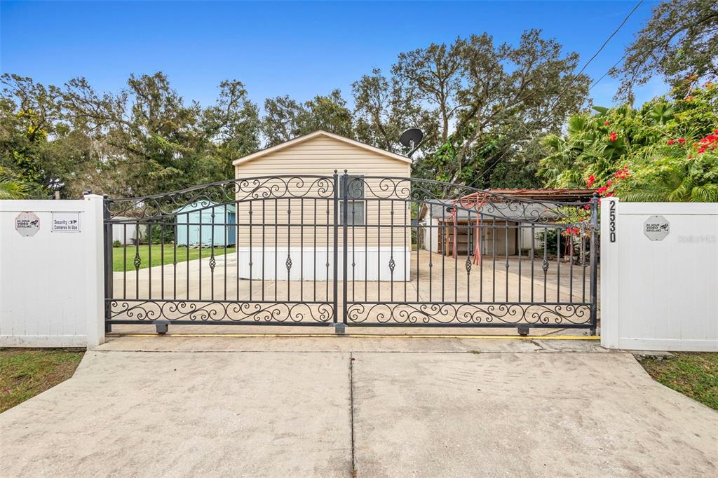 A beige mobile home sits behind a black wrought iron gate and white fence — 2530 CRESAP STREET, LAKELAND, FL