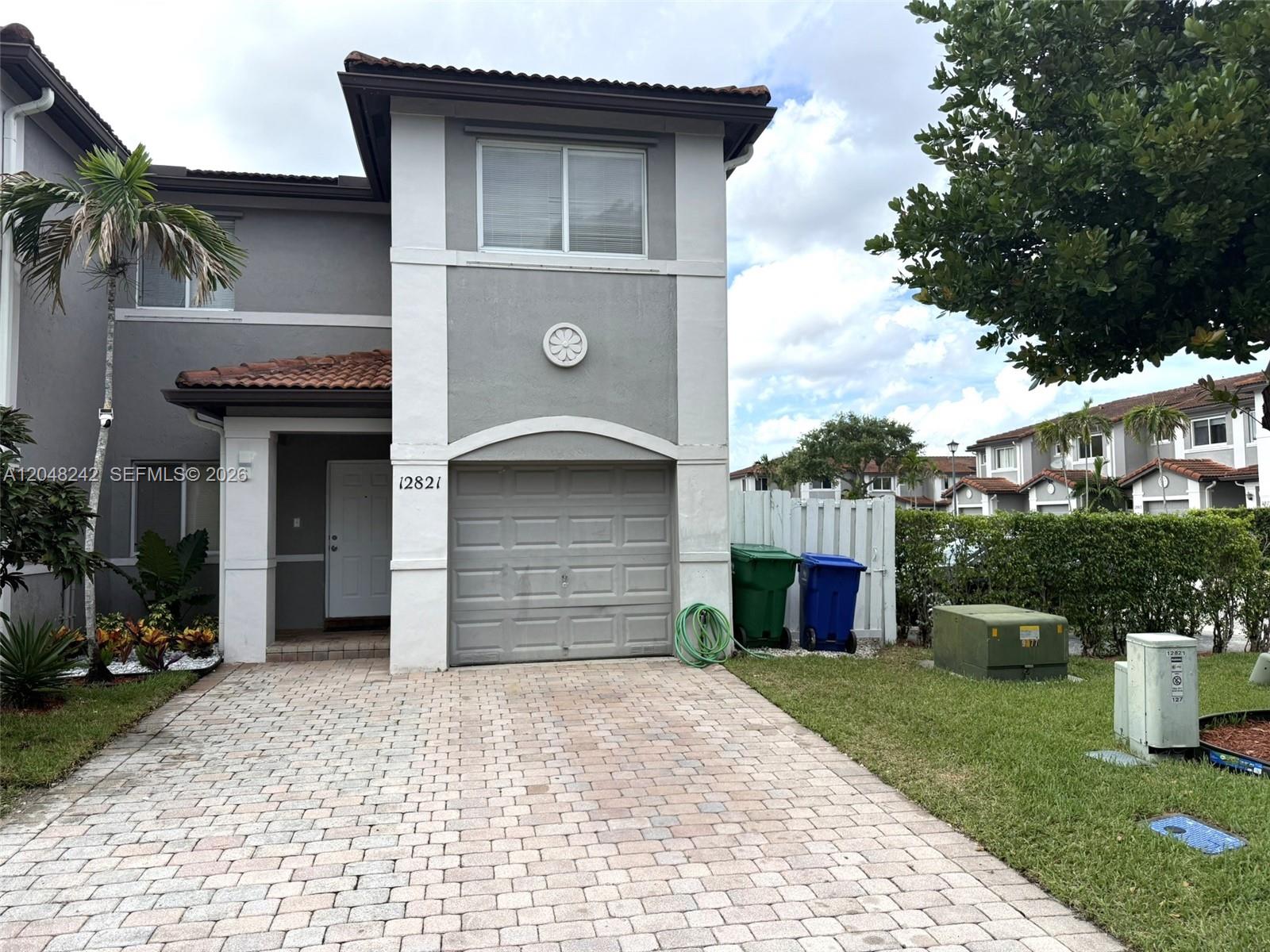 A two-story townhouse with a gray stucco exterior, a brick paver driveway, and a garage — 12821 SW 29th St, Miramar FL 33027, MIRAMAR, FL