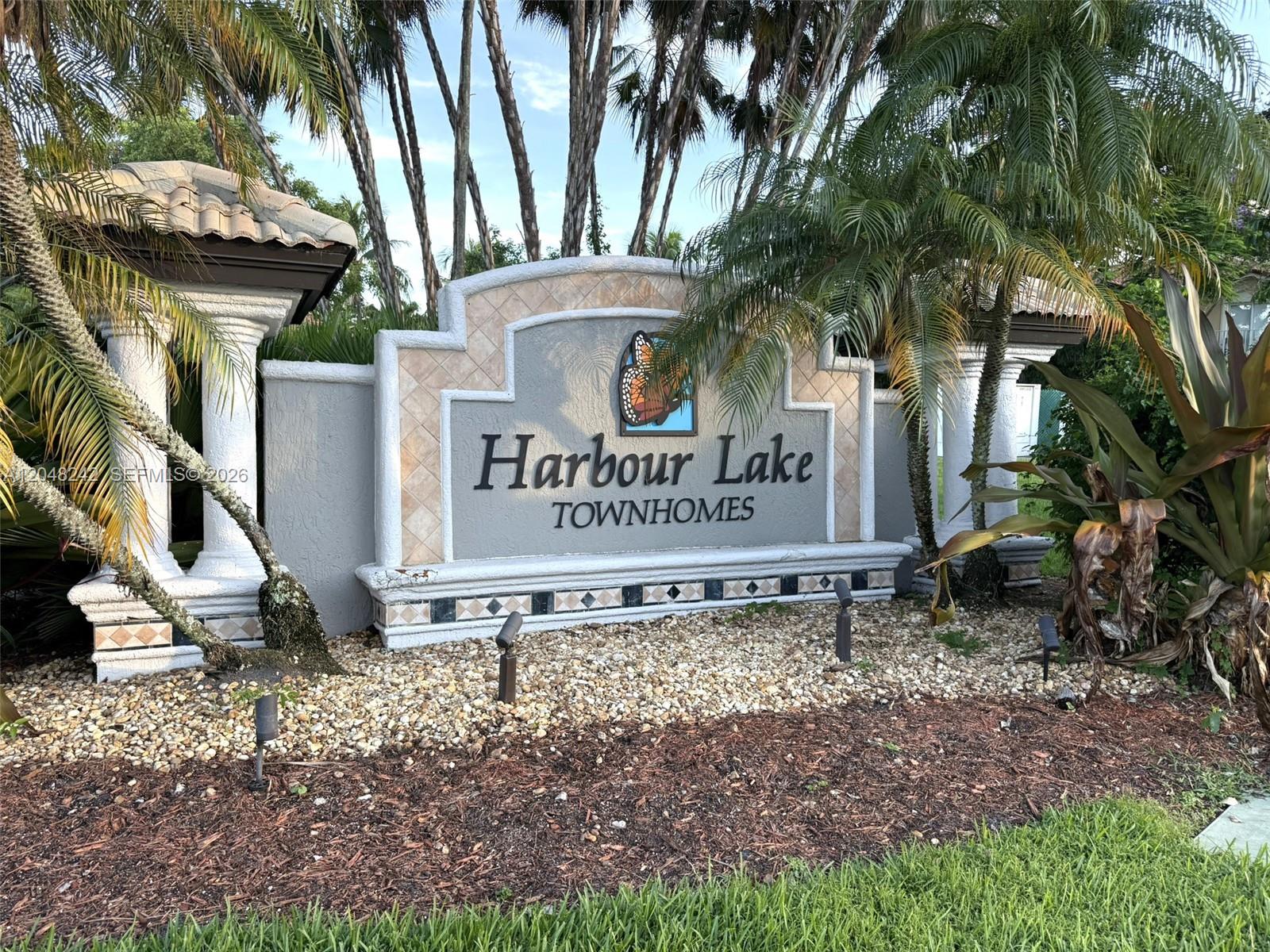 A stone monument sign for Harbour Lake Townhomes stands surrounded by palm trees and landscaping — 12821 SW 29th St, Miramar FL 33027, MIRAMAR, FL