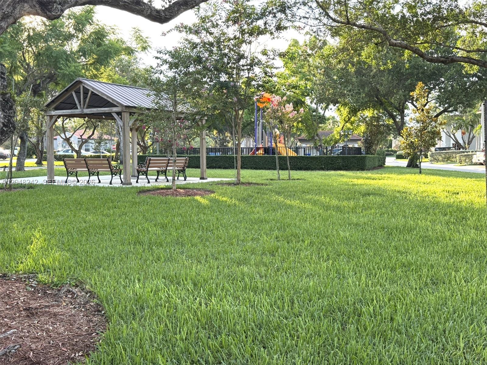 A wooden gazebo with benches sits on a grassy lawn near a playground — 12821 SW 29th St, Miramar FL 33027, MIRAMAR, FL