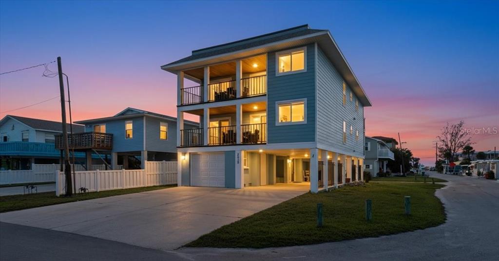 A three-story light blue house on stilts features two levels of covered balconies at dusk — 2518 AVENUE B, BRADENTON BEACH, FL