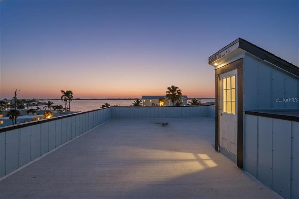 A rooftop deck with a small access structure overlooks a sunset over the water — 2518 AVENUE B, BRADENTON BEACH, FL