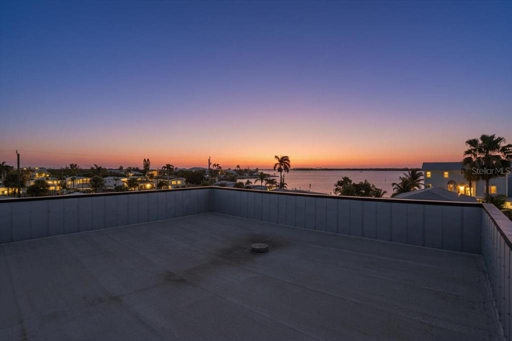A flat rooftop deck overlooks a coastal sunset with palm trees and water in the distance — 2518 AVENUE B, BRADENTON BEACH, FL