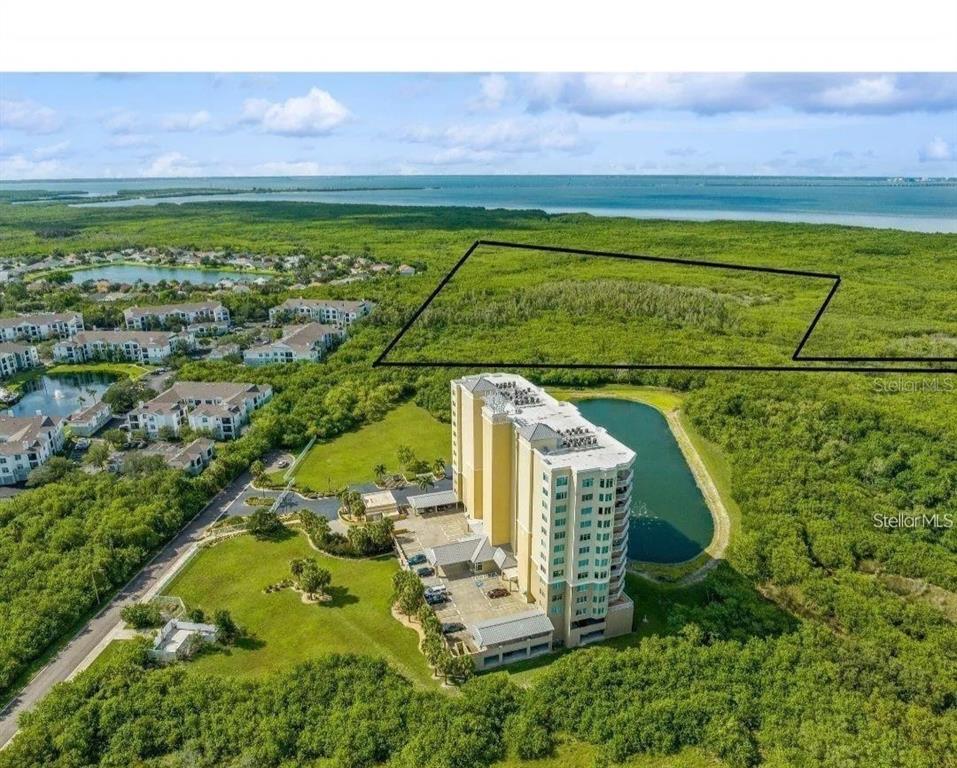 An aerial view shows a tall apartment building next to a pond and undeveloped land — 0 MANGROVE CAY LANE NE, ST PETERSBURG, FL