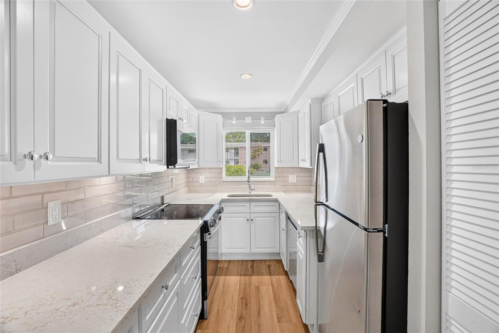 A galley kitchen features white cabinets, light-colored countertops, stainless steel appliances, and wood-look flooring — 4570 OVERLOOK DRIVE NE UNIT 175, ST PETERSBURG, FL