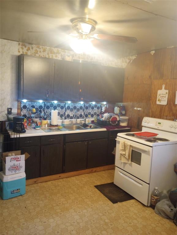 A kitchen features dark cabinets, a white stove, a patterned backsplash, and light-colored flooring — 14016 N. HWY 301, THONOTOSASSA, FL