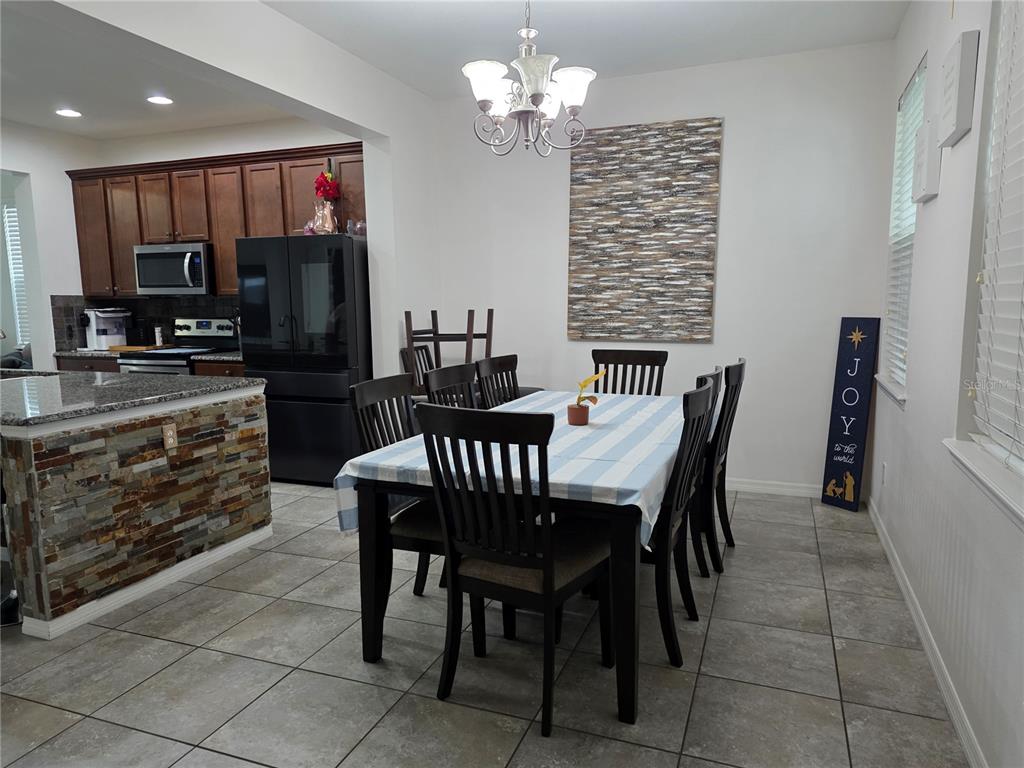 A dining area features a table with six chairs, a chandelier, and a stone-accented kitchen island — 12749 GARRIDAN AVENUE, WINDERMERE, FL
