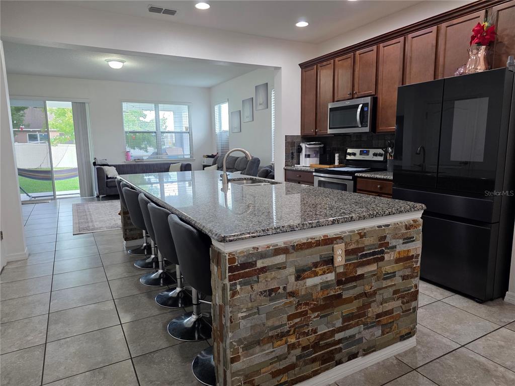 A kitchen features a stone-faced island with bar seating, dark wood cabinets, and black appliances — 12749 GARRIDAN AVENUE, WINDERMERE, FL