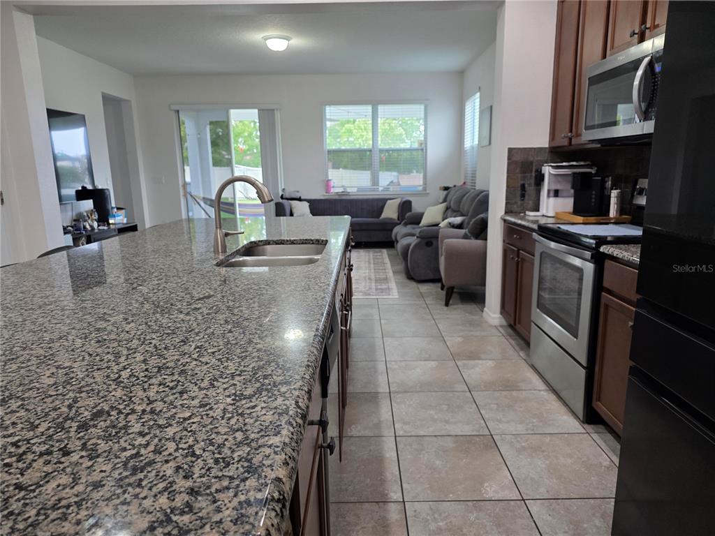 A kitchen with a granite island and stainless steel appliances overlooks a living area — 12749 GARRIDAN AVENUE, WINDERMERE, FL