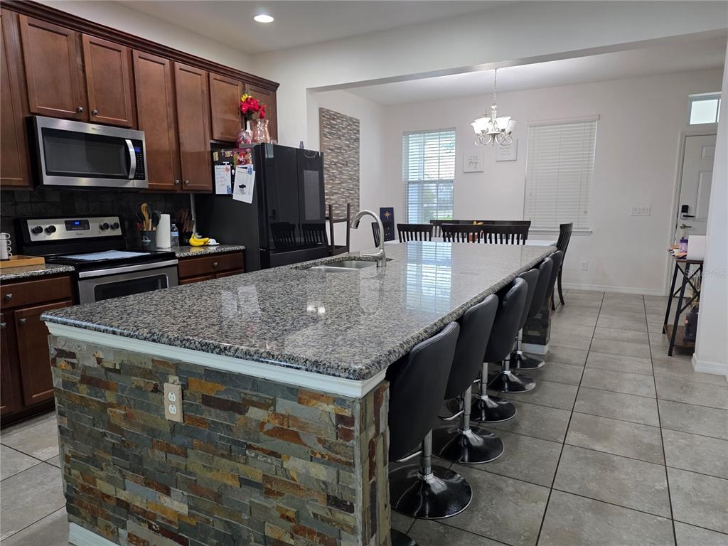 A kitchen features a large granite-topped island with stone veneer siding and black bar stools — 12749 GARRIDAN AVENUE, WINDERMERE, FL