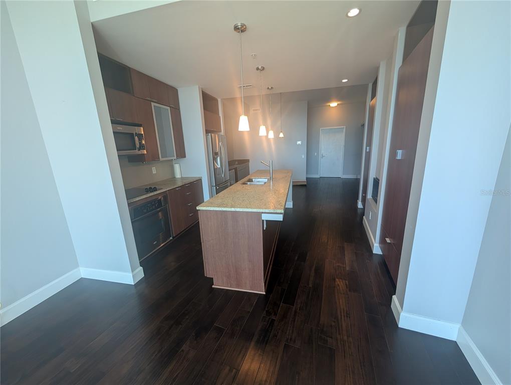 A modern kitchen features dark wood cabinetry, a granite-topped island, and dark hardwood flooring — 912 CHANNELSIDE DRIVE UNIT 2803, TAMPA, FL