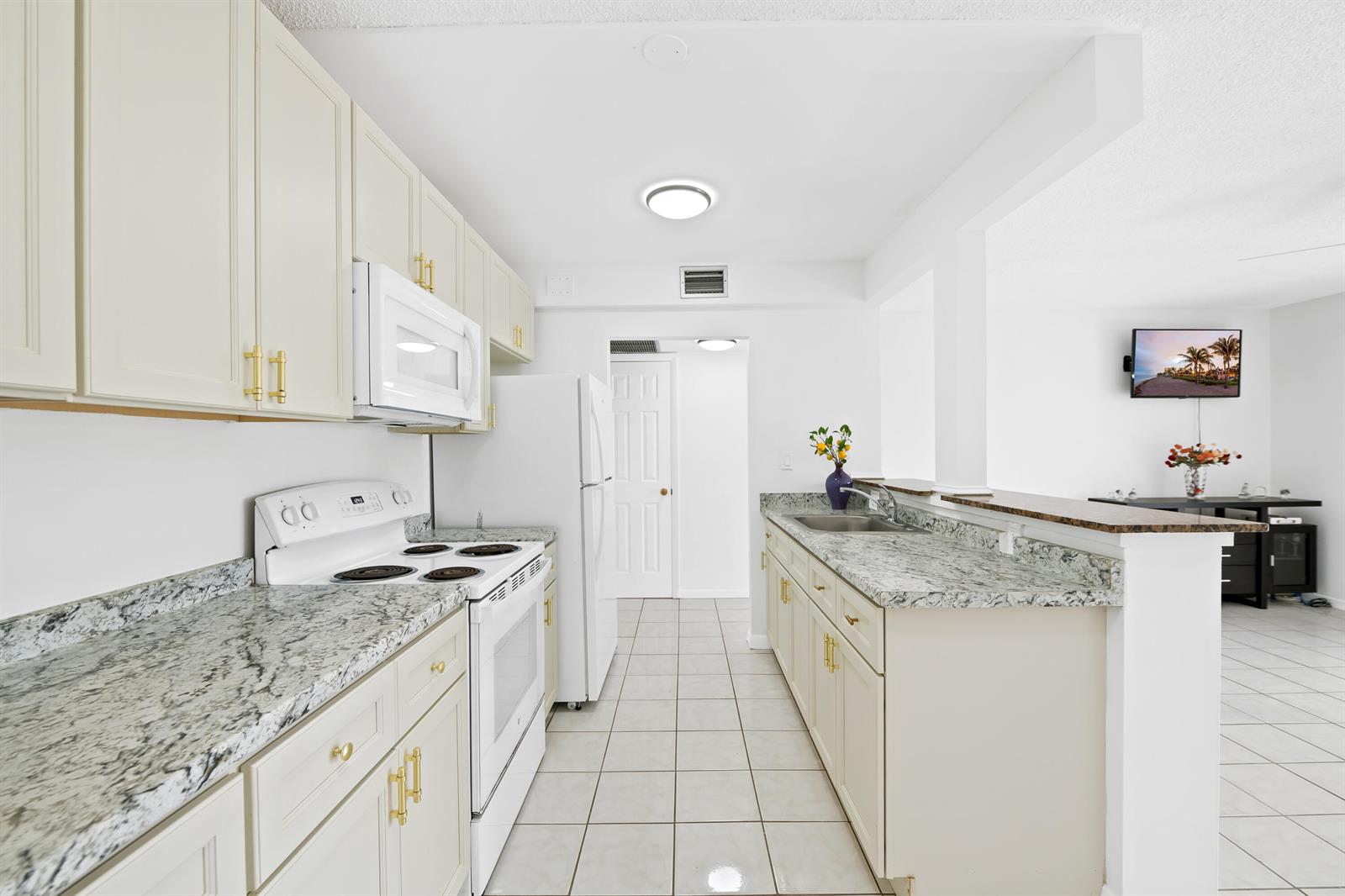 A galley kitchen features white cabinets, granite countertops, and tile flooring — 5190 E Sabal Palm Boulevard # 209, Tamarac FL 33319, TAMARAC, FL