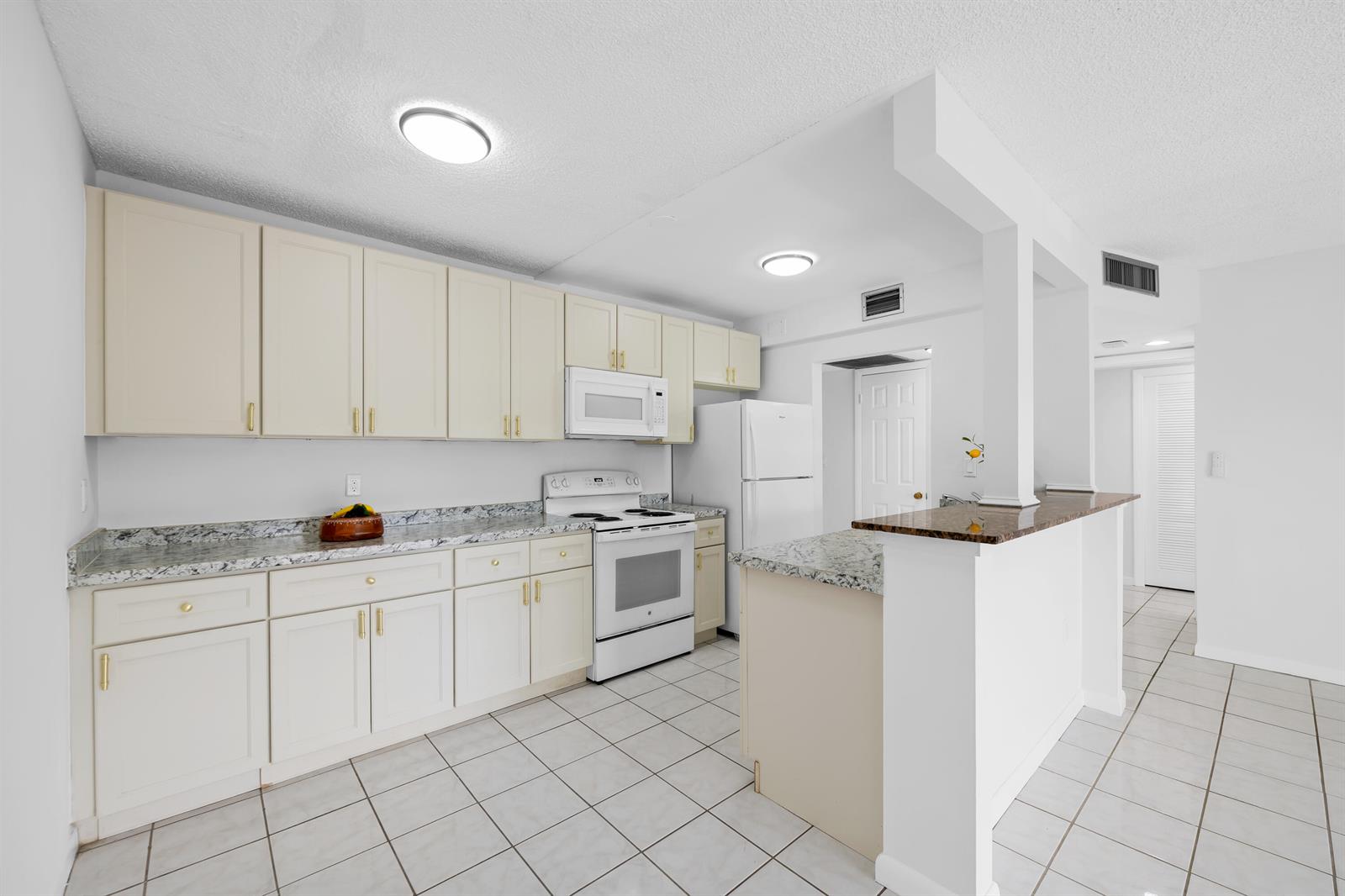 A kitchen with white cabinets, granite countertops, white appliances, and light-colored tile flooring — 5190 E Sabal Palm Boulevard # 209, Tamarac FL 33319, TAMARAC, FL