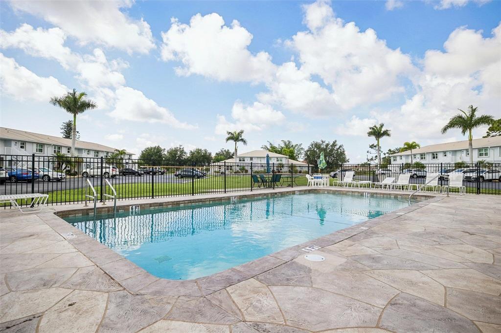 An outdoor swimming pool with a stone deck is enclosed by a black metal fence — 26485 RAMPART BOULEVARD UNIT A27, PUNTA GORDA, FL