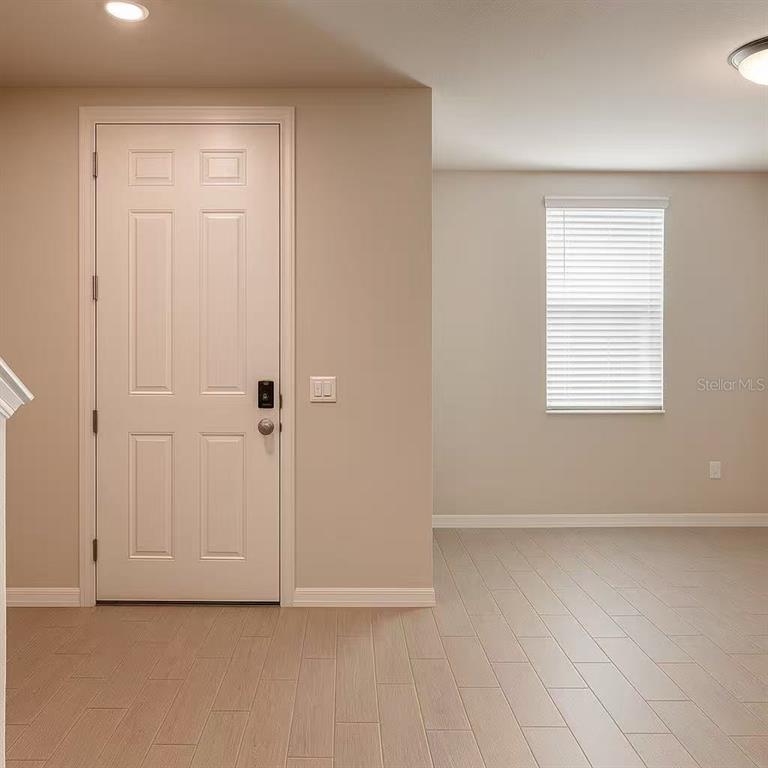 An interior view showing a white front door, a window with blinds, and light-colored flooring — 17351 MILLION LAKES COURT, CLERMONT, FL