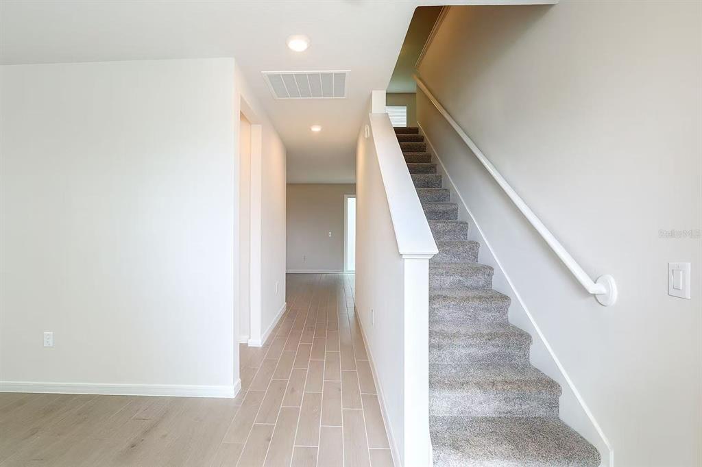 A hallway with light-colored tile flooring leads toward a staircase with gray carpet — 17351 MILLION LAKES COURT, CLERMONT, FL