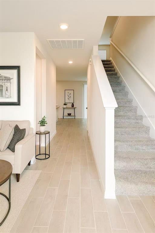 A hallway with light wood-look tile flooring leads to a staircase with gray carpeting — 17351 MILLION LAKES COURT, CLERMONT, FL