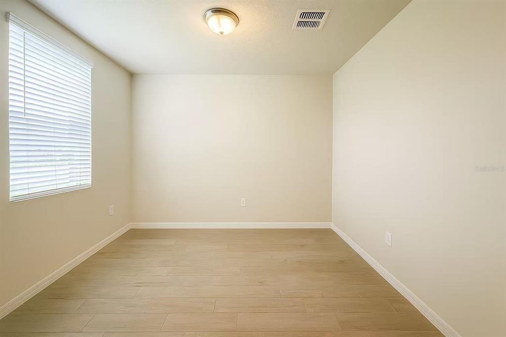 An empty room with light wood-look flooring, beige walls, and a window with white blinds — 17351 MILLION LAKES COURT, CLERMONT, FL