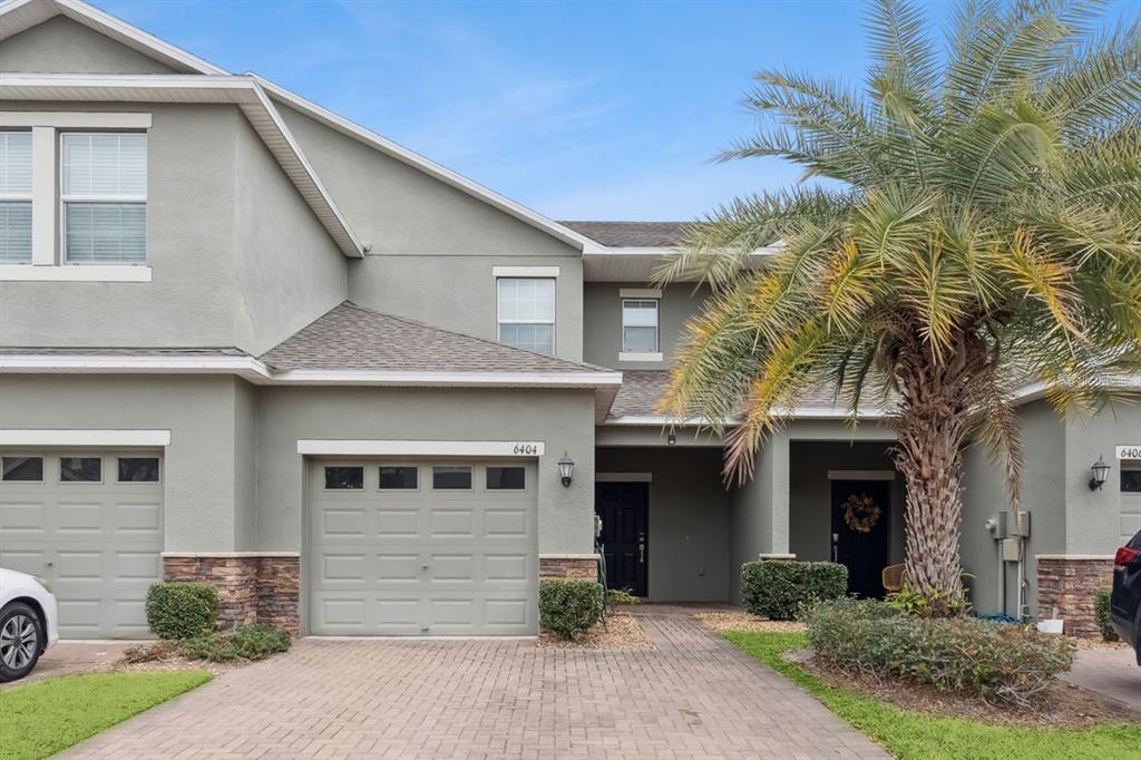 A two-story townhouse exterior features a single-car garage, stone accents, and a palm tree — 6404 TORRINGTON CIRCLE, LAKELAND, FL