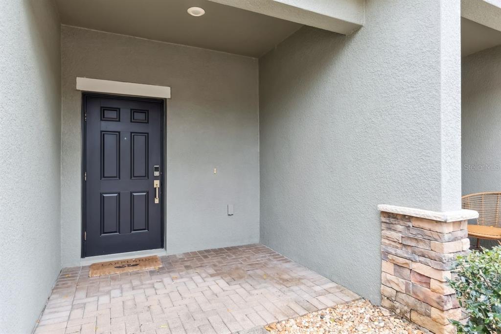 A covered entryway features a dark front door, a brick paver floor, and stone accents — 6404 TORRINGTON CIRCLE, LAKELAND, FL