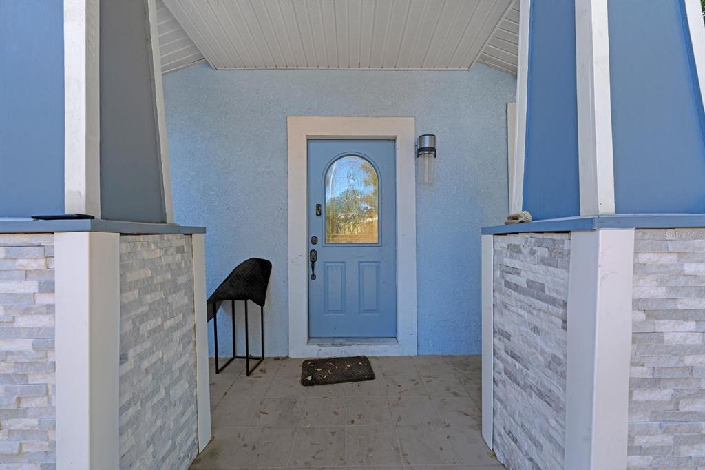 A covered front porch features a light blue door, stone-tiled walls, and tiled flooring — 4204 N MARGUERITE STREET, TAMPA, FL
