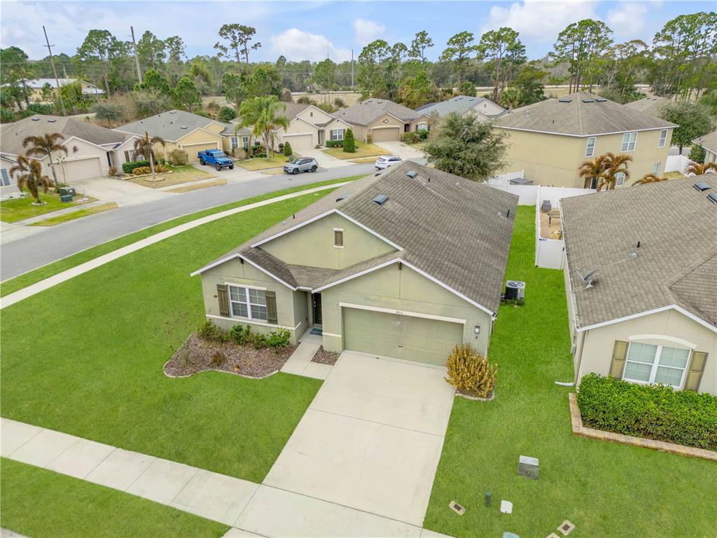 An aerial view shows a single-story suburban house with a green exterior and concrete driveway — 402 PINK CORAL LANE, NEW SMYRNA BEACH, FL