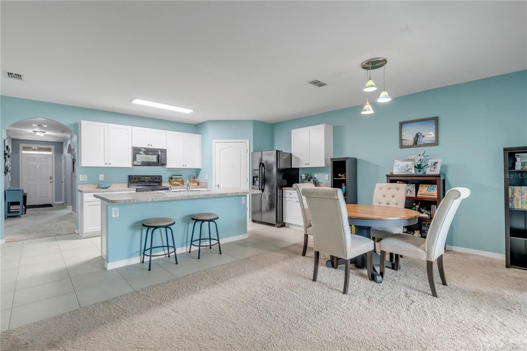 A kitchen with white cabinets, a breakfast bar, and an adjacent dining area with carpet — 402 PINK CORAL LANE, NEW SMYRNA BEACH, FL