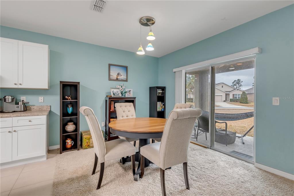 A dining area features a round table, upholstered chairs, light blue walls, and sliding glass doors — 402 PINK CORAL LANE, NEW SMYRNA BEACH, FL