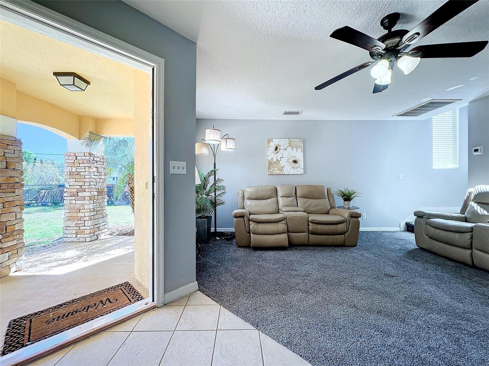 A living room with gray carpet and leather furniture opens to a covered stone patio — 2560 Franklin Avenue, Winter Park FL 32789, WINTER PARK, FL