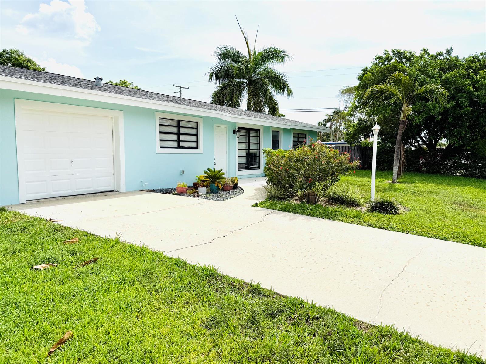 A light blue single-story house with a white garage door, driveway, and palm trees — 477 NE 35th Street, Boca Raton FL 33431, BOCA RATON, FL