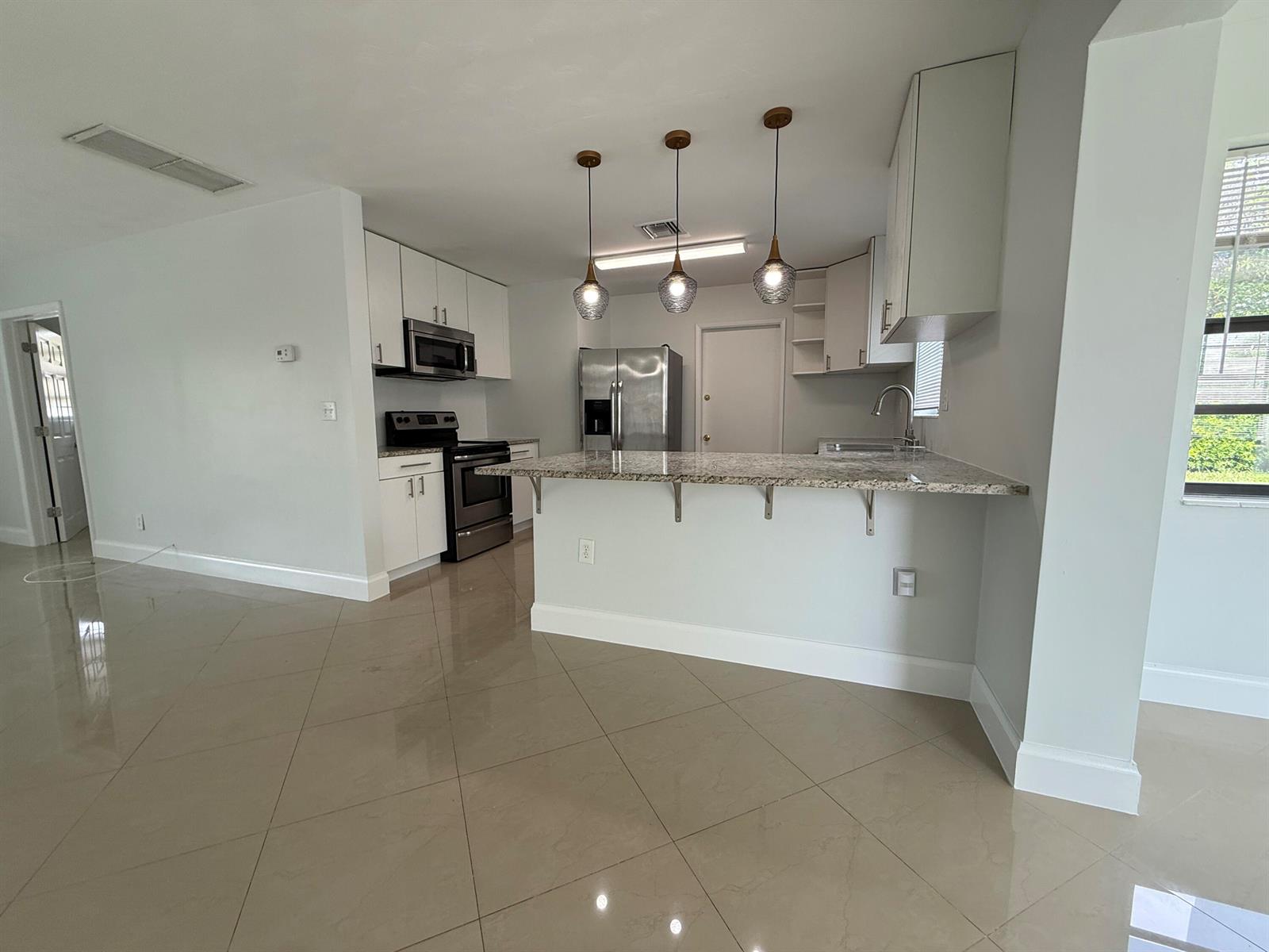 A kitchen features white cabinets, granite countertops, stainless steel appliances, and a breakfast bar — 477 NE 35th Street, Boca Raton FL 33431, BOCA RATON, FL
