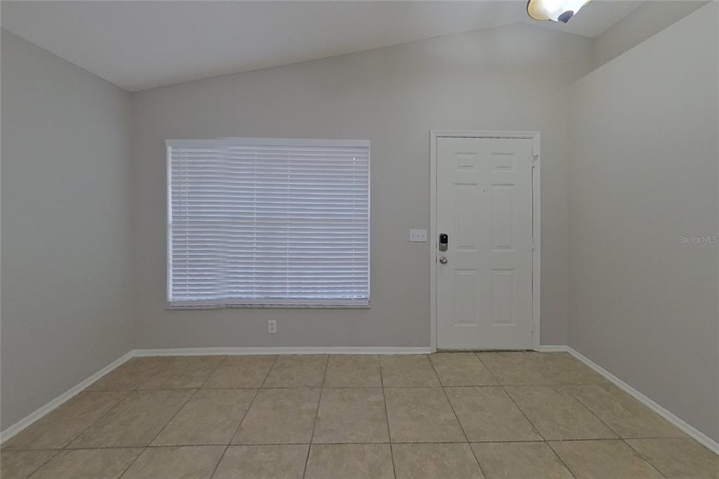 A room with light gray walls, tile flooring, a window with blinds, and a front door — 1248 E CLEVELAND AVENUE, APOPKA, FL