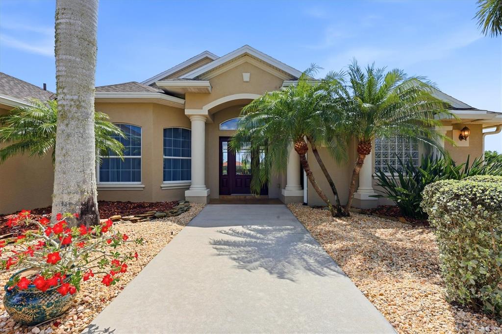 A tan stucco house features a concrete walkway leading to a covered front entryway — 13561 BLAKE DRIVE, PORT CHARLOTTE, FL