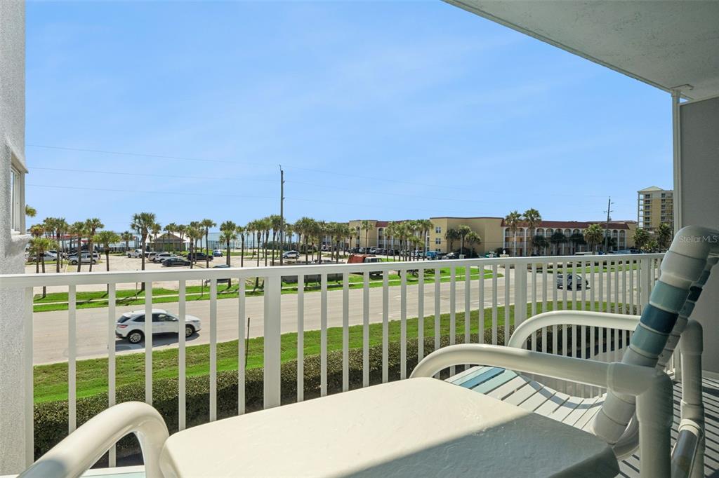 A balcony with white railings overlooks a parking lot, palm trees, and a distant building — 3700 S ATLANTIC AVENUE UNIT 309, NEW SMYRNA BEACH, FL