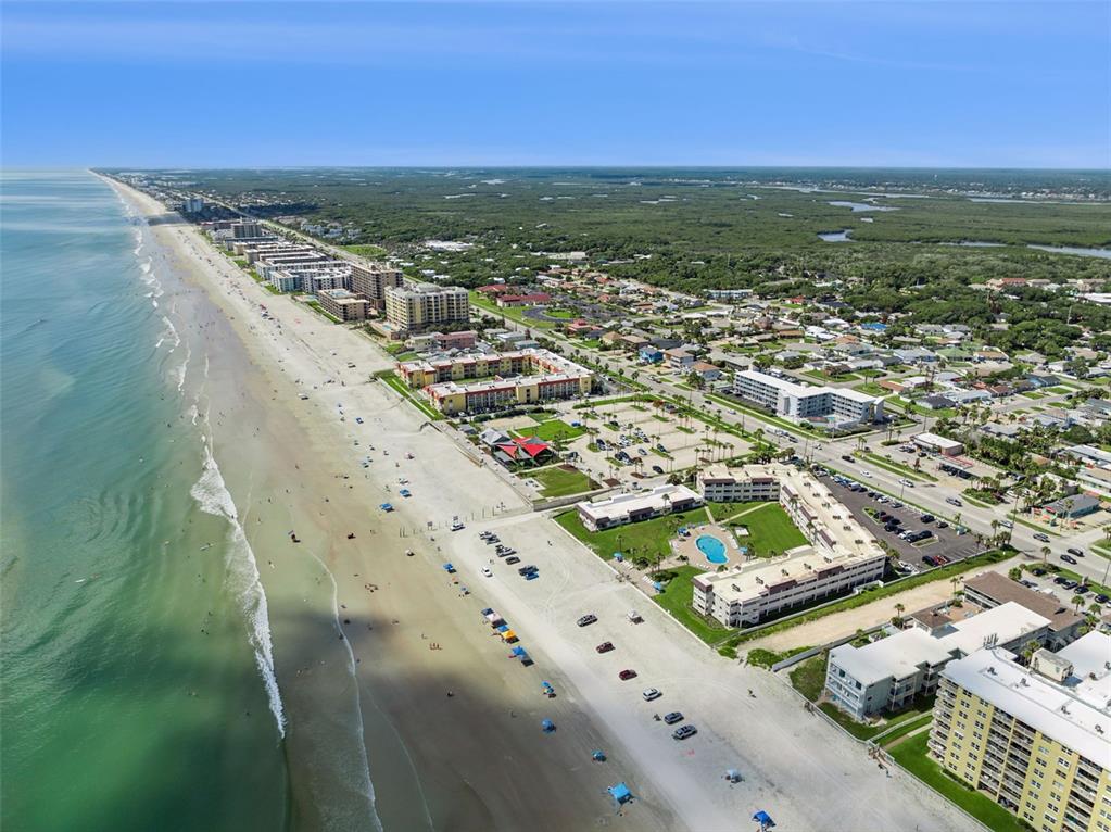 Aerial view of a sandy beach lined with multi-story residential buildings and a parking lot — 3700 S ATLANTIC AVENUE UNIT 309, NEW SMYRNA BEACH, FL